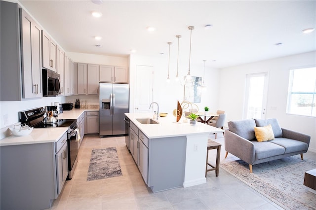 kitchen with appliances with stainless steel finishes, decorative light fixtures, sink, gray cabinetry, and a center island with sink