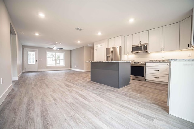 kitchen featuring a center island, appliances with stainless steel finishes, light stone countertops, light hardwood / wood-style floors, and white cabinets