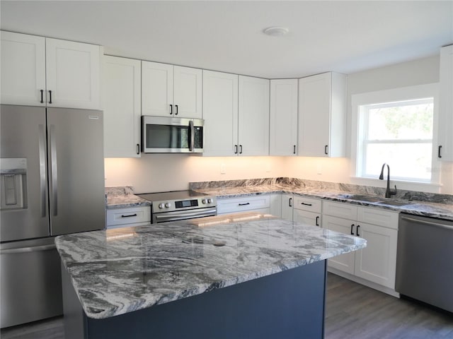 kitchen with sink, a kitchen island, stainless steel appliances, light stone countertops, and white cabinets