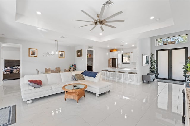 living room featuring french doors, ceiling fan, and a tray ceiling