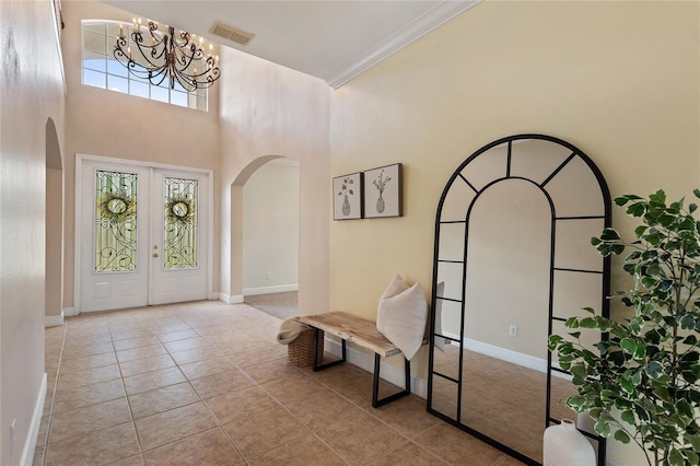 tiled entrance foyer with french doors, a healthy amount of sunlight, crown molding, and a high ceiling