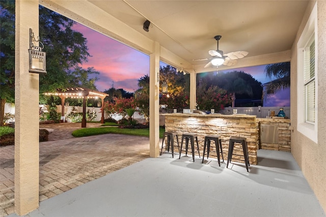 patio terrace at dusk featuring ceiling fan and exterior bar