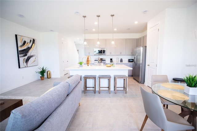 interior space featuring light tile patterned floors, appliances with stainless steel finishes, a kitchen island with sink, hanging light fixtures, and a kitchen breakfast bar