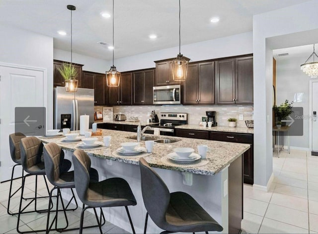 kitchen with stainless steel appliances, a breakfast bar area, a center island with sink, and decorative light fixtures