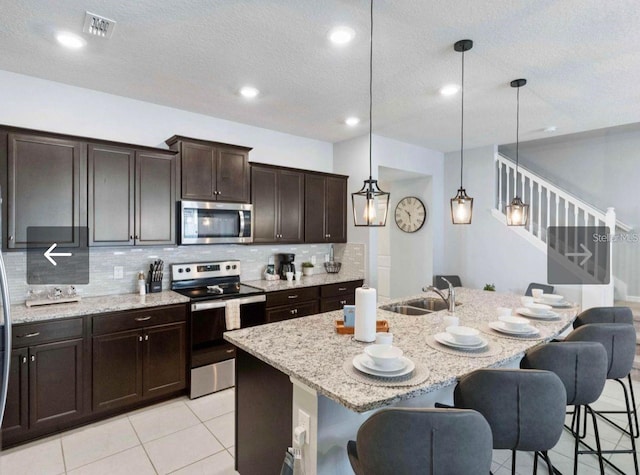 kitchen with decorative light fixtures, stainless steel appliances, an island with sink, and a kitchen bar