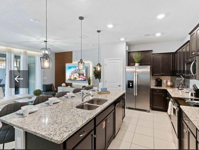 kitchen with pendant lighting, sink, a kitchen island with sink, stainless steel appliances, and dark brown cabinets