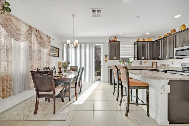 kitchen featuring appliances with stainless steel finishes, hanging light fixtures, dark brown cabinetry, light stone countertops, and a healthy amount of sunlight