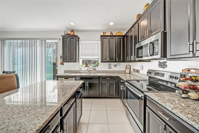 kitchen with dark brown cabinetry, sink, light stone counters, light tile patterned floors, and appliances with stainless steel finishes