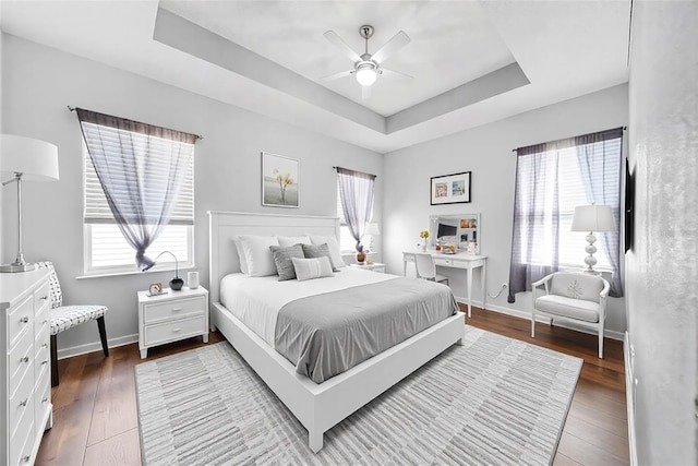 bedroom with multiple windows, wood-type flooring, ceiling fan, and a tray ceiling