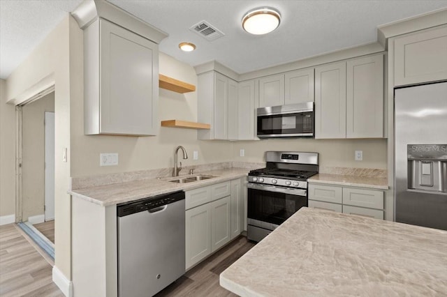 kitchen featuring stainless steel appliances, sink, light stone counters, and light hardwood / wood-style flooring