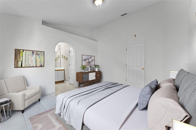 bedroom with lofted ceiling, connected bathroom, and light tile patterned floors