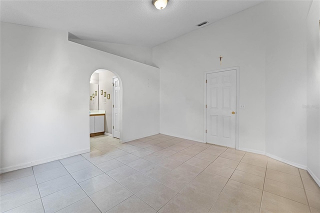 tiled empty room featuring vaulted ceiling and a textured ceiling