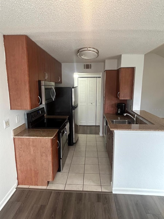 kitchen with sink, a textured ceiling, light wood-type flooring, kitchen peninsula, and stainless steel appliances