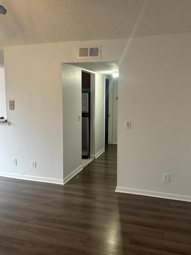 empty room with dark wood-type flooring and a textured ceiling