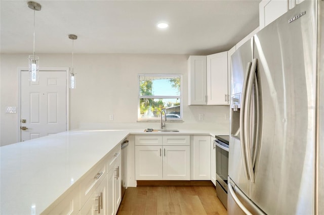 kitchen featuring pendant lighting, sink, white cabinets, stainless steel appliances, and light wood-type flooring