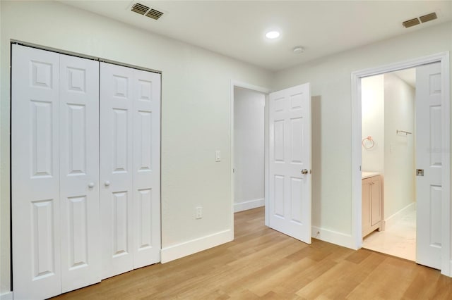 unfurnished bedroom with ensuite bathroom, light wood-type flooring, and a closet