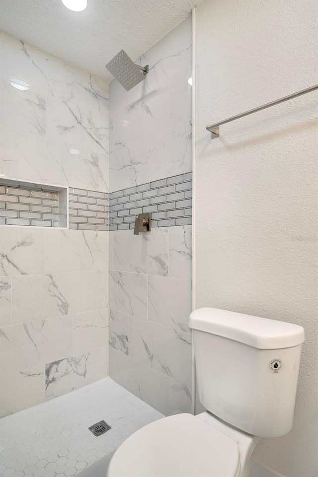 bathroom featuring tiled shower, toilet, and a textured ceiling