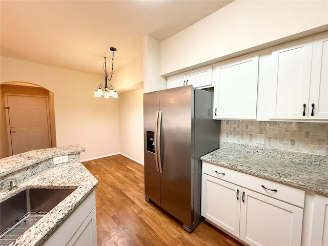 kitchen featuring white cabinets, light stone countertops, hanging light fixtures, and stainless steel fridge