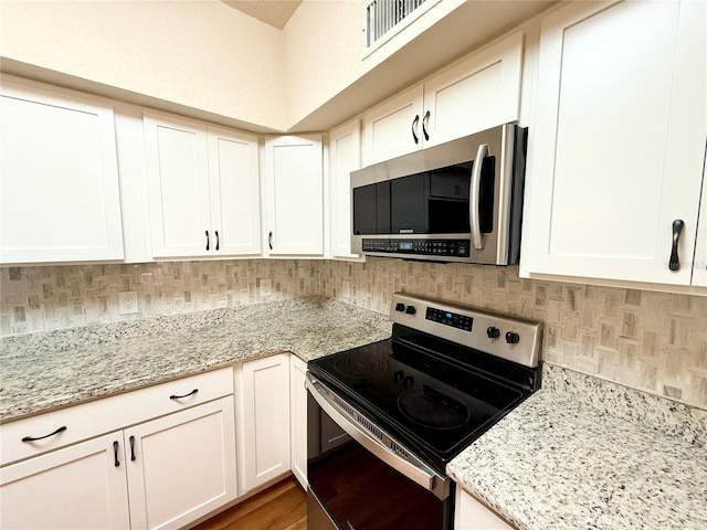 kitchen with tasteful backsplash, white cabinetry, light stone counters, stainless steel appliances, and light hardwood / wood-style flooring