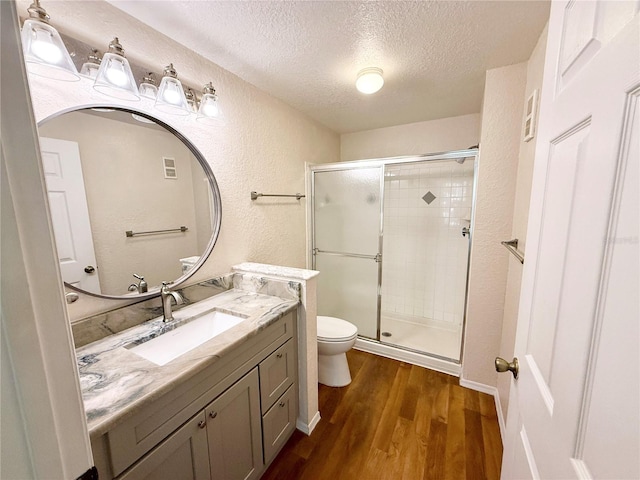 bathroom with hardwood / wood-style flooring, a shower with door, vanity, a textured ceiling, and toilet