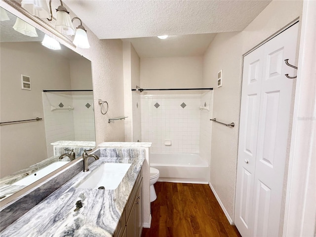 full bathroom with wood-type flooring, tiled shower / bath combo, vanity, toilet, and a textured ceiling