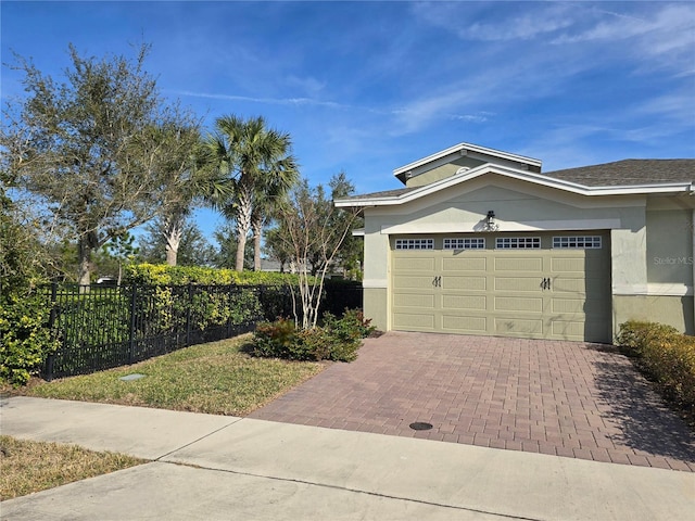 view of side of property featuring decorative driveway, fence, an attached garage, and stucco siding