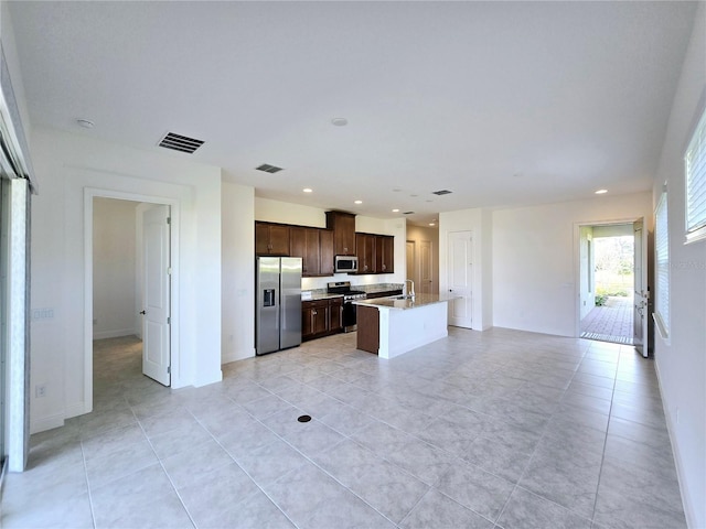 kitchen with sink, light tile patterned floors, a kitchen island with sink, stainless steel appliances, and dark brown cabinetry