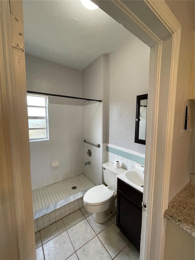 bathroom featuring tile walls, a tile shower, vanity, a textured ceiling, and toilet