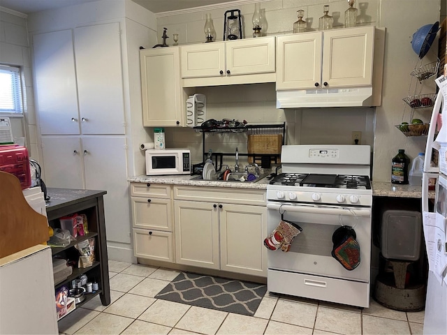 kitchen with light tile patterned flooring, sink, light stone counters, and white appliances