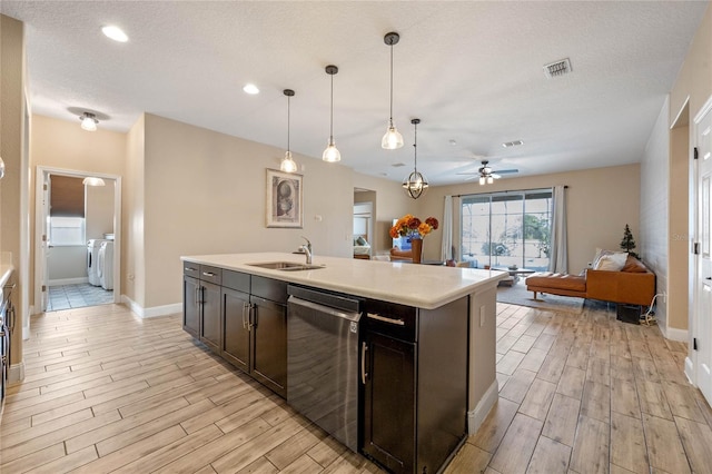 kitchen featuring decorative light fixtures, sink, stainless steel dishwasher, washing machine and dryer, and a center island with sink