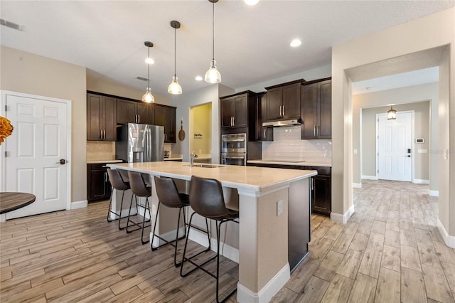 kitchen featuring appliances with stainless steel finishes, decorative light fixtures, an island with sink, a kitchen breakfast bar, and dark brown cabinetry