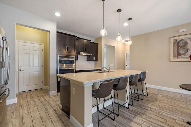 kitchen with pendant lighting, tasteful backsplash, sink, dark brown cabinetry, and a center island with sink