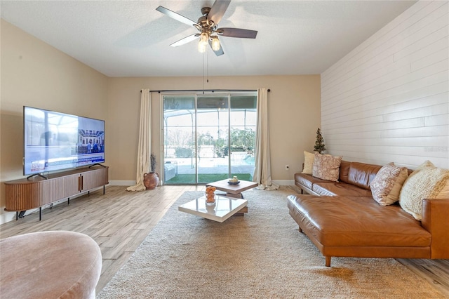 living room with ceiling fan, a textured ceiling, and light hardwood / wood-style floors