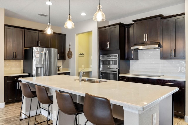 kitchen featuring appliances with stainless steel finishes, sink, decorative light fixtures, and an island with sink