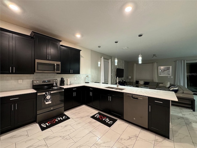 kitchen featuring sink, appliances with stainless steel finishes, kitchen peninsula, pendant lighting, and decorative backsplash