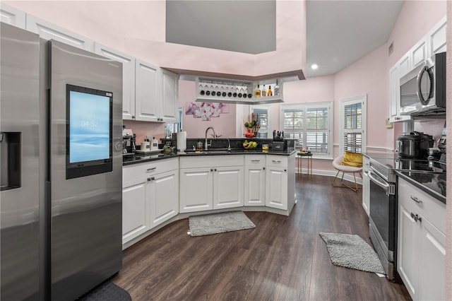 kitchen with dark wood-type flooring, sink, appliances with stainless steel finishes, kitchen peninsula, and white cabinets