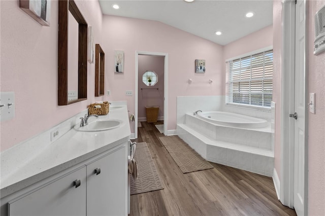 bathroom with lofted ceiling, hardwood / wood-style floors, vanity, and tiled bath