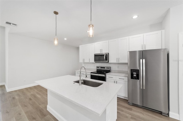 kitchen featuring stainless steel appliances, an island with sink, white cabinets, and decorative light fixtures