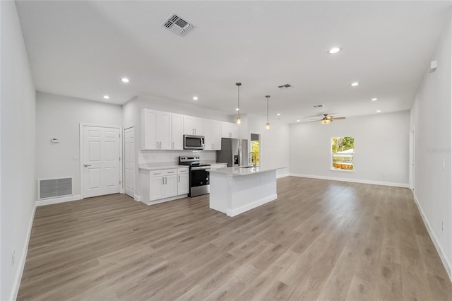 kitchen with appliances with stainless steel finishes, white cabinets, hanging light fixtures, a center island, and light wood-type flooring