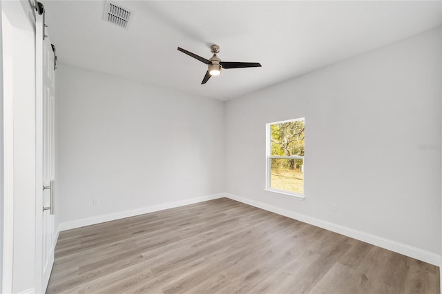 spare room featuring light hardwood / wood-style flooring, a barn door, and ceiling fan