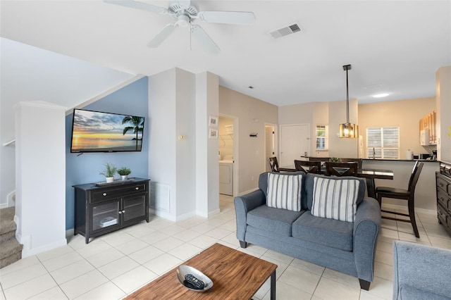 living room with washer / dryer, ceiling fan with notable chandelier, and light tile patterned floors