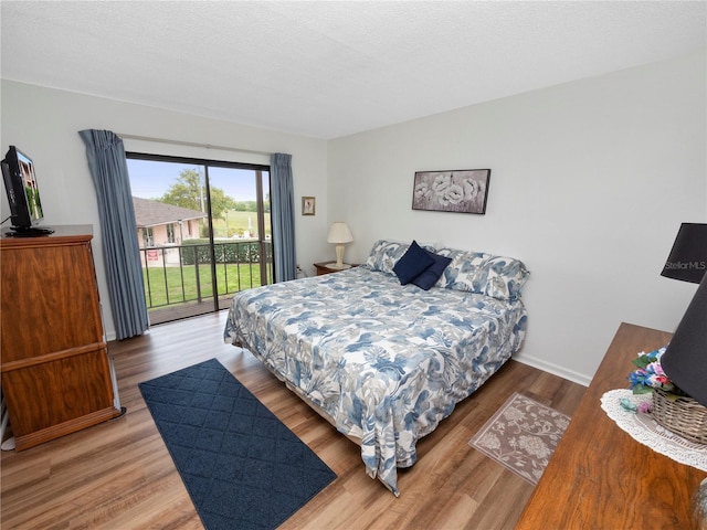 bedroom with access to exterior, wood-type flooring, and a textured ceiling