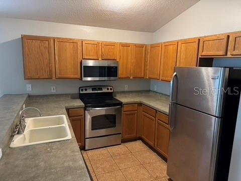 kitchen with vaulted ceiling, appliances with stainless steel finishes, sink, light tile patterned floors, and a textured ceiling