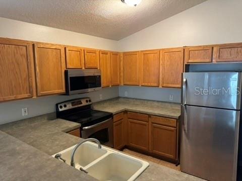 kitchen with lofted ceiling, stainless steel appliances, sink, and a textured ceiling