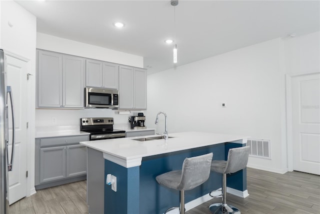 kitchen featuring appliances with stainless steel finishes, pendant lighting, sink, light hardwood / wood-style floors, and a center island with sink