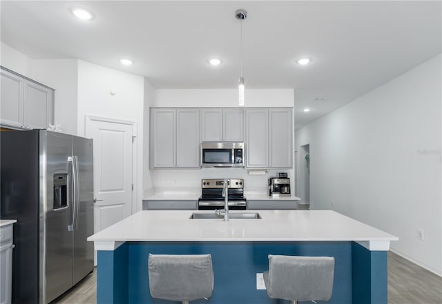 kitchen with a breakfast bar, appliances with stainless steel finishes, a center island with sink, decorative light fixtures, and light wood-type flooring