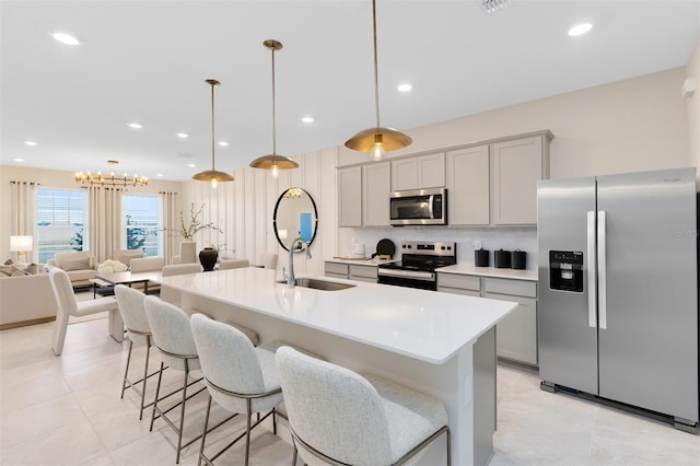 kitchen featuring stainless steel appliances, gray cabinets, an island with sink, and hanging light fixtures