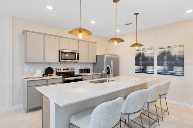 kitchen featuring appliances with stainless steel finishes, decorative light fixtures, a center island with sink, and gray cabinetry