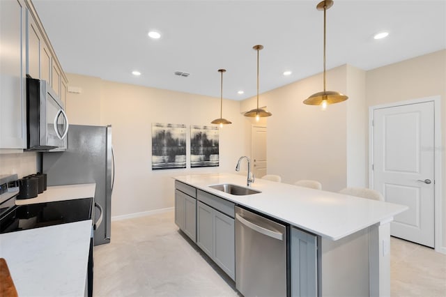 kitchen featuring pendant lighting, sink, gray cabinetry, a kitchen island with sink, and stainless steel appliances