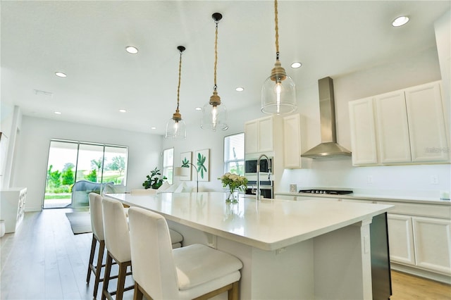 kitchen featuring a large island, decorative light fixtures, light hardwood / wood-style floors, and wall chimney exhaust hood